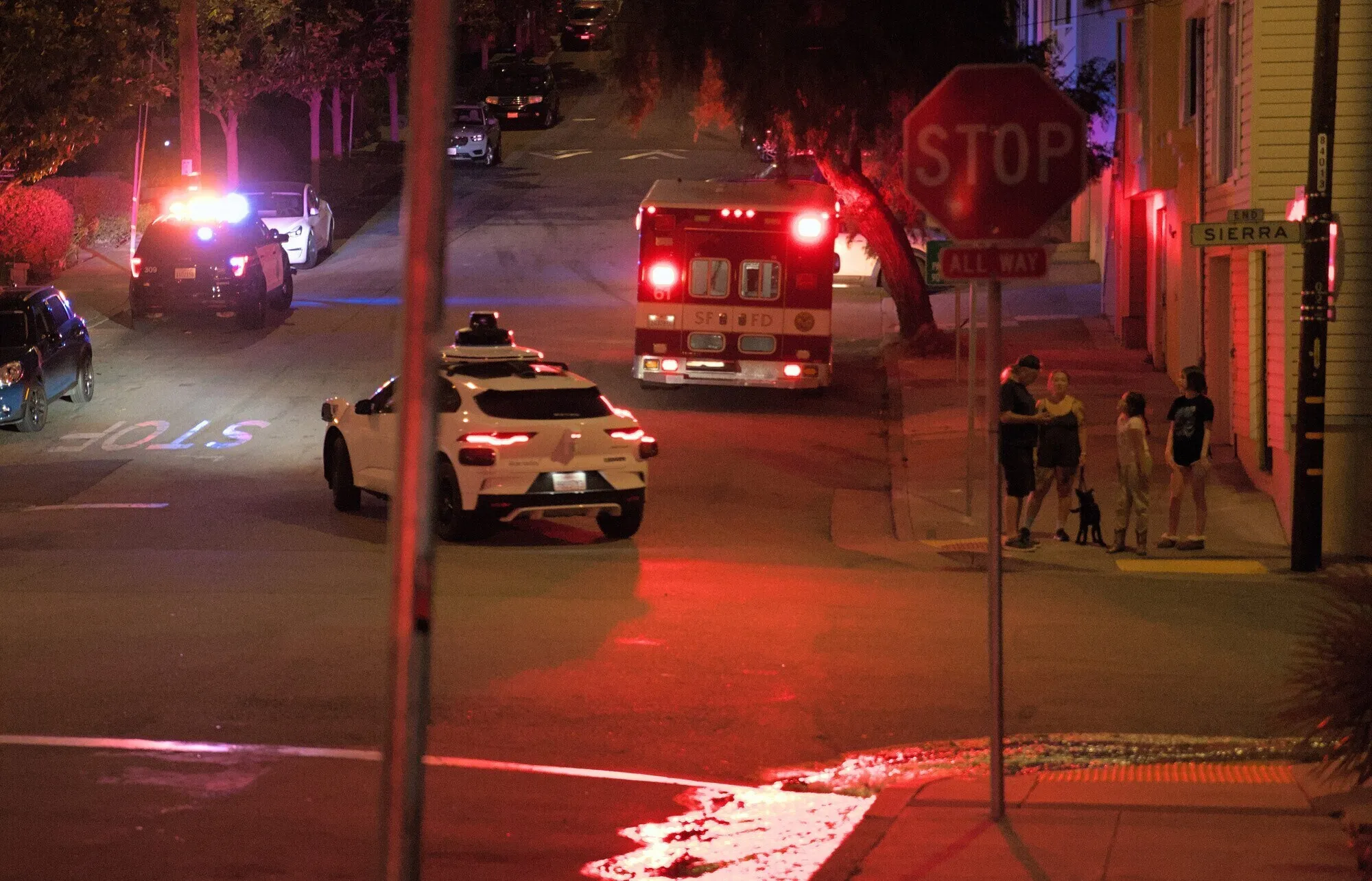 Sep 30th, 2024: Water from SFFD hoses flow down the gutter on Missouri St. Concerned neighbors watch and an autonomous Waymo drives by.
