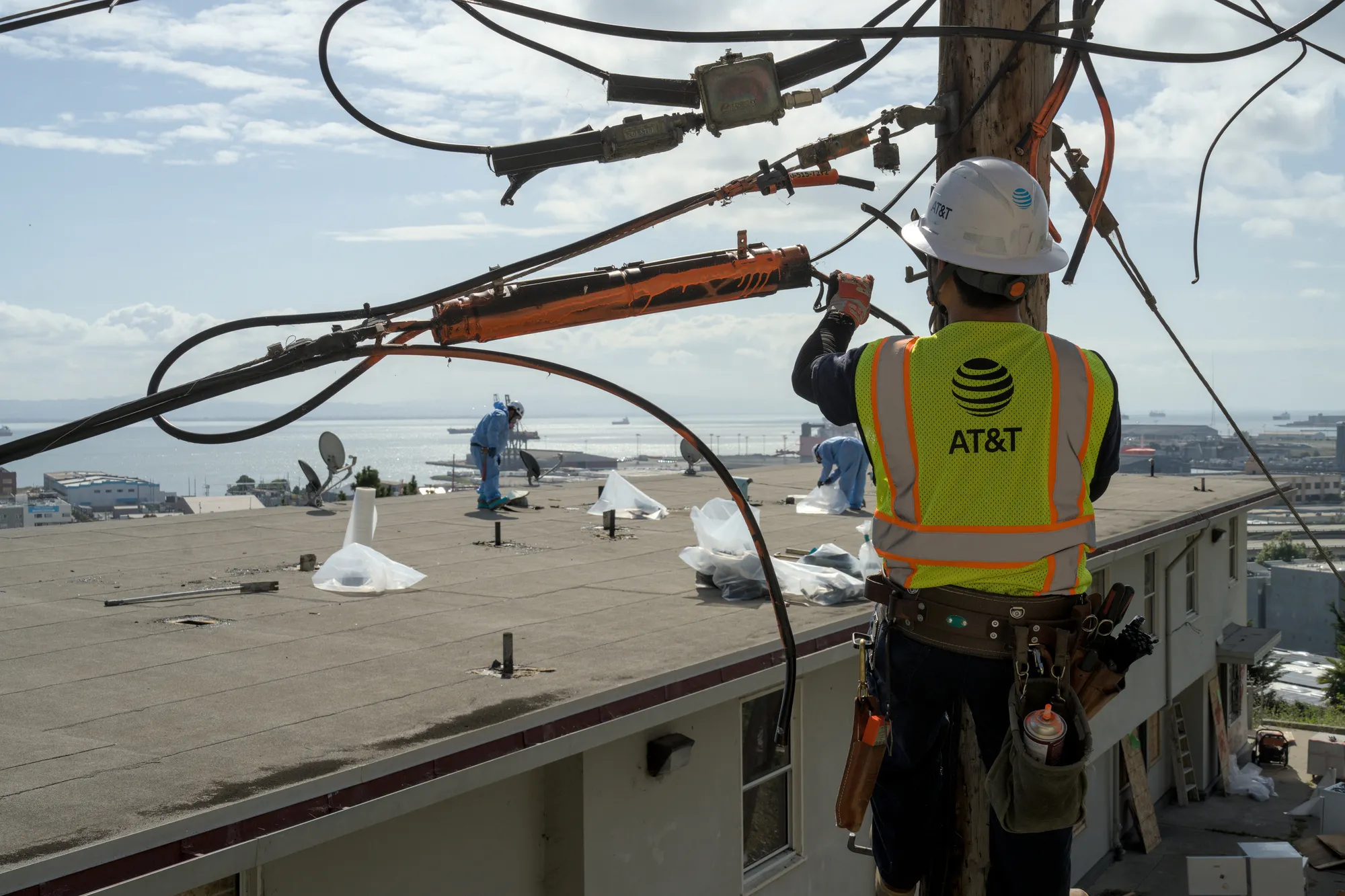Apr 27th, 2026: An AT&T employee climbs a telephone pole while an asbestos abatement crew works on a roof in Potrero Annex.