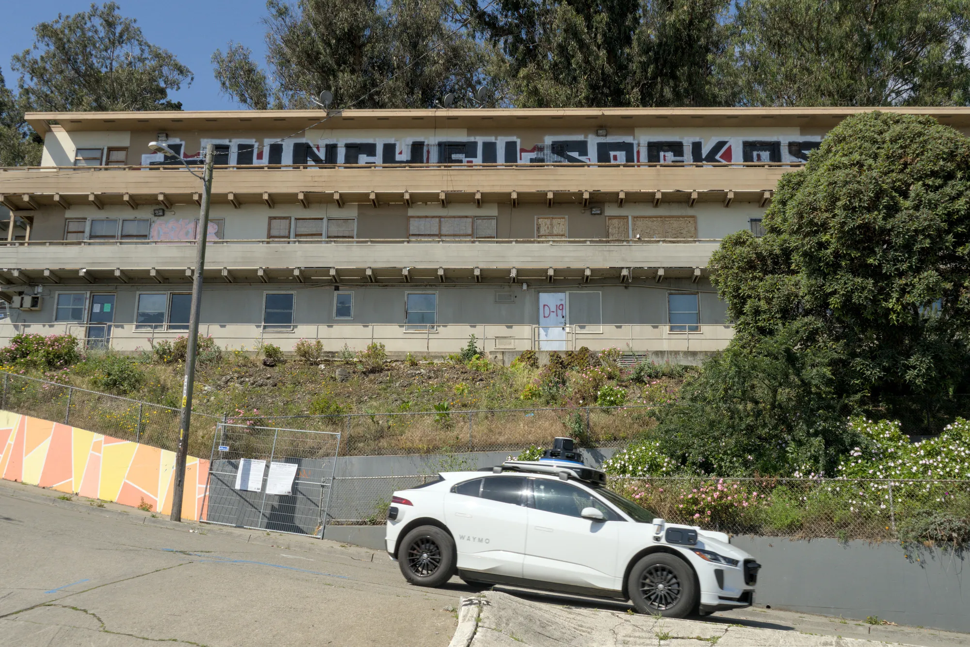 May 6th, 2026: An autonomous Waymo drives past a graffiti-covered building in the Potrero Annex.