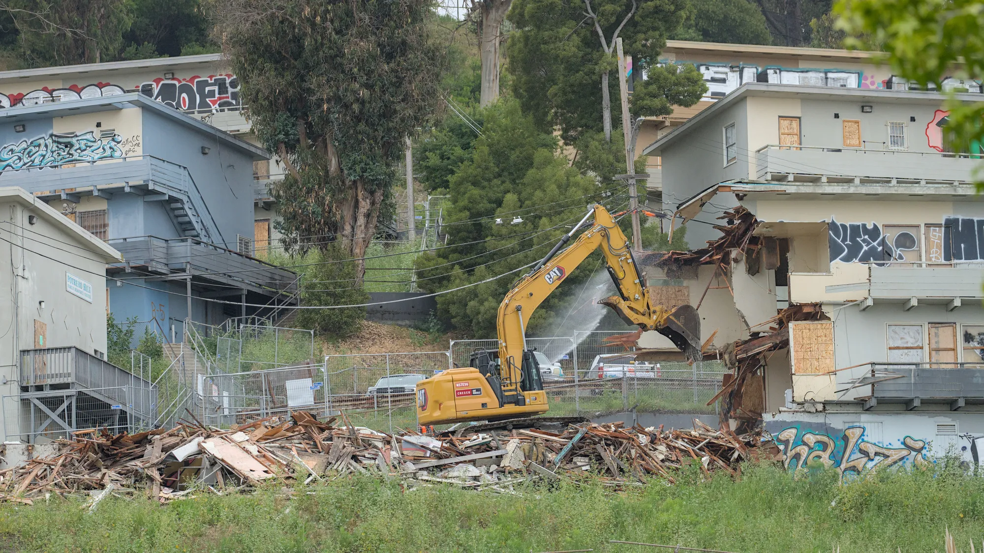May 12th, 2026: An excavator demolishes a building in Potrero Annex while a water hose minimizes dust.